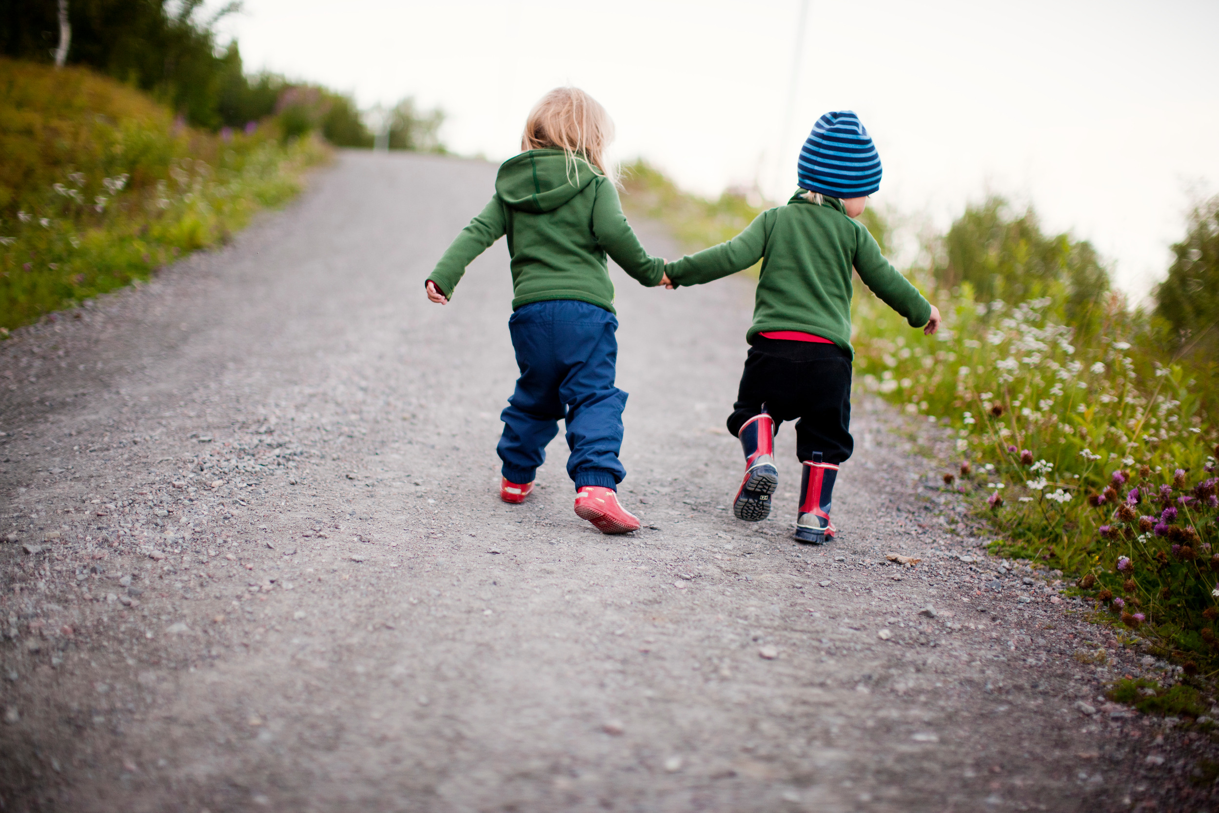 Två små barn går hand i hand på en grusväg.
