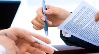 Två personer i kavaj vid ett bord håller i pennor och papper.