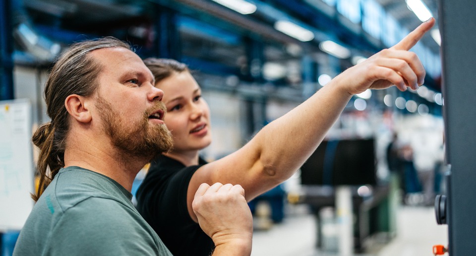 Två personer tittar på en stor skärm i en industrilokal.