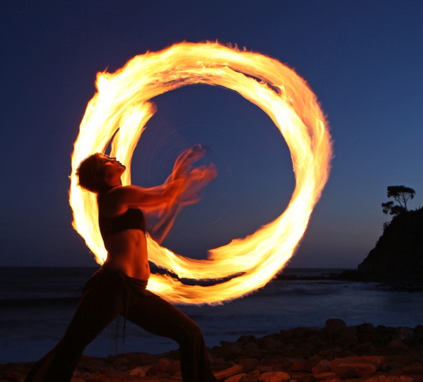 Person som dansar med eld på en strand i skymningen.