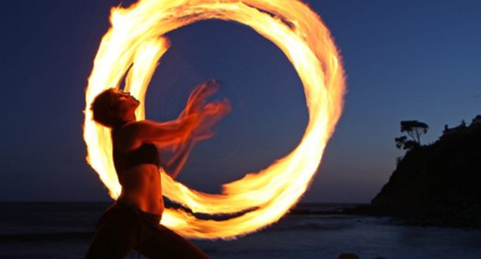 Person som dansar med eld på en strand i skymningen.
