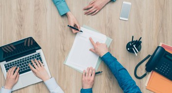 Tre personers händer på arbetsbord under ett arbetsmöte