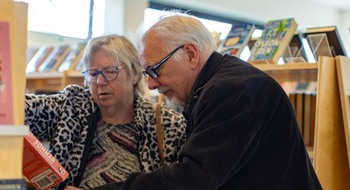 Äldre person letar böcker på bibliotek.