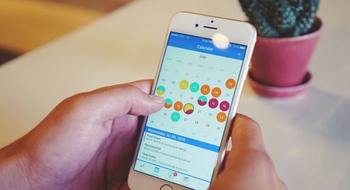 Händer håller i en mobiltelefon med en digital kalender.