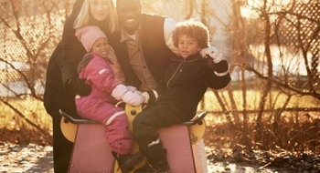 En familj poserar vid ett gungdjur på en lekplats.