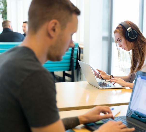 Två personer som sitter vid bord och knappar på sina laptops.
