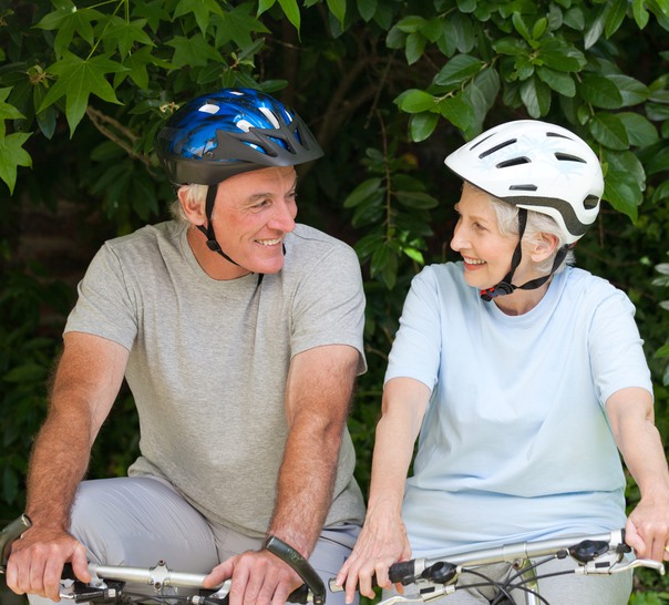 Två seniora personer på cyklar med grönska runt om. 