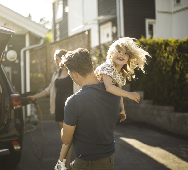 En vuxen bär ett skrattande barn vid en bil.