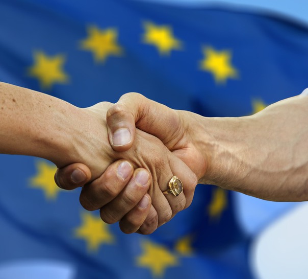Närbild på två personer som skakar hand framför EU-flaggan.