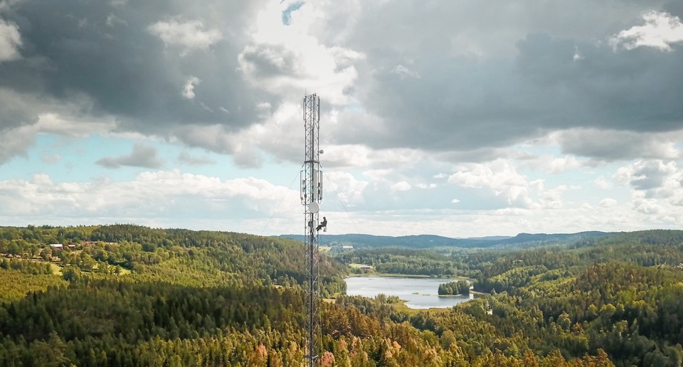 Telecommunication manual high worker engineer installing new 4g, 5g LTE antenna on tall mobile base station (communication tower) in the middle of european forest. Working at height. Telecommunication masts and towers are typically tall structures designed to support antennas for telecommunications and broadcasting. Drone point of view.