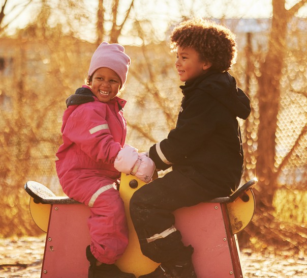 Två barn sitter på en gunghäst på en lekplats. 