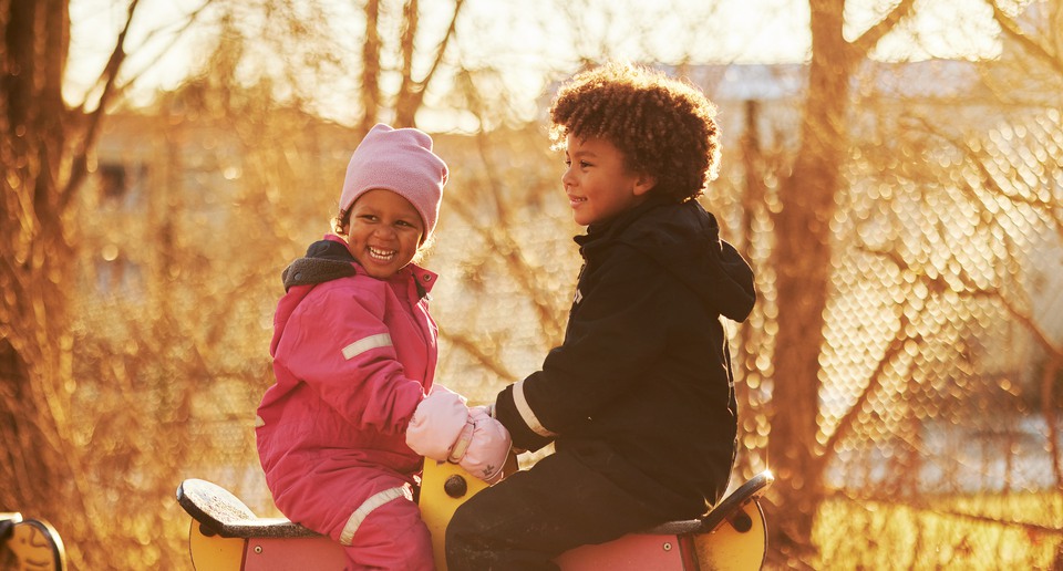 Två barn sitter på en gunghäst på en lekplats. 