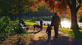 En vuxen promenerar i en park med två barn och en hund.