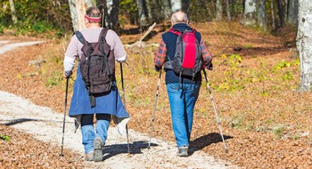 Två äldre personer vandrar med ryggsäckar och stavar.