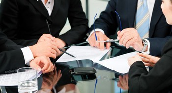 Flera personer i kavaj sitter vid ett bord med papper.