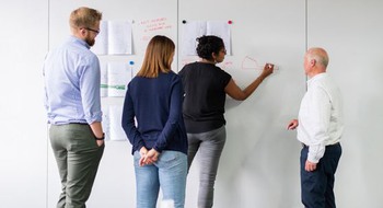 Fyra personer står framför en vägg och ritar.