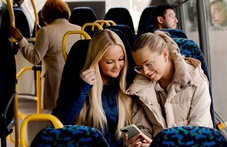 Två tjejer tittar på en telefon på bussen
