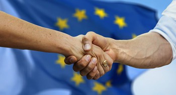Närbild på två personer som skakar hand framför EU-flaggan.