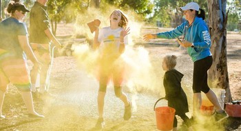 En familj leker utomhus med pulverfärg, solen skiner.