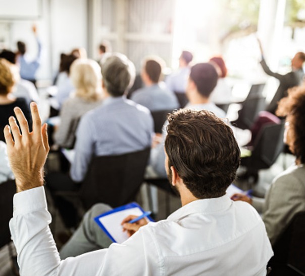 Personer i en publik där några räcker upp handen.