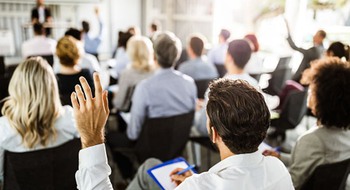 Personer i en publik där några räcker upp handen.