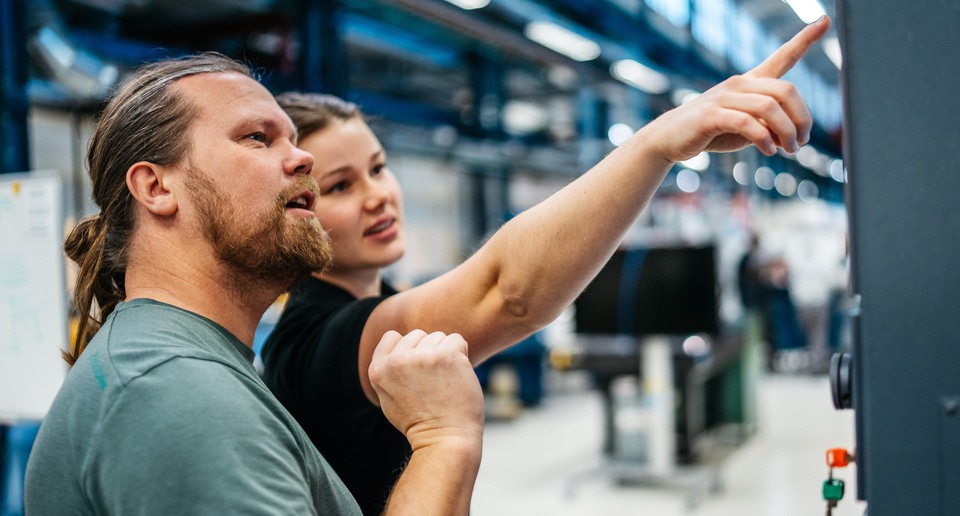 Två personer tittar på en stor skärm i en industrilokal.