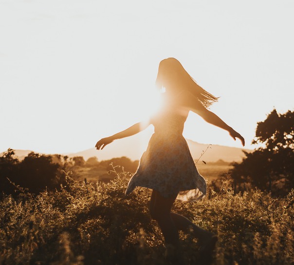 Person som dansar på äng i motljus.