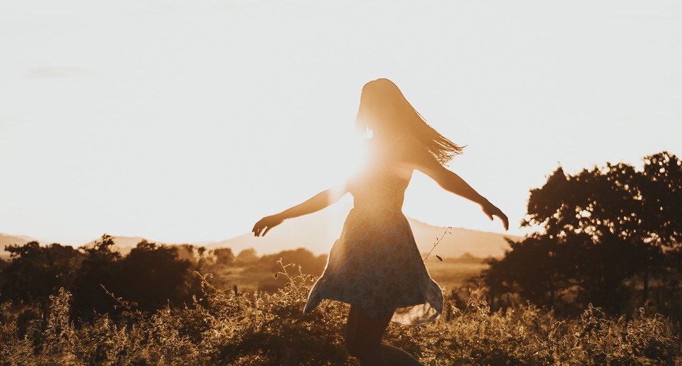 Person som dansar på äng i motljus.