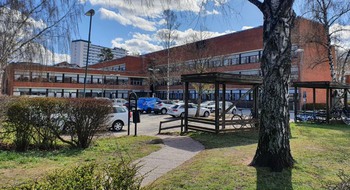 Byggnad med flera huskroppar med parkerade bilar framför.