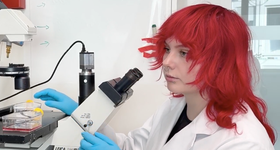 Porträtt av forskaren Marina Peltonen vid ett mikroskop. 