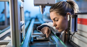 Närbild på person i vit rock vid maskin.