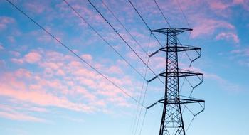 Kraftledning sedd underifrån mot blå himmel med moln.