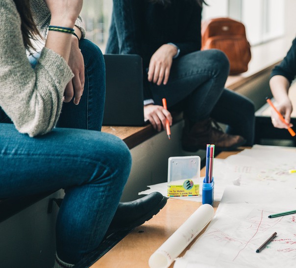 Unga personer sitter på en fönsterbräda framför ett bord med papper och pennor.