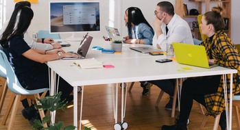 Några personer som sitter vi ett bord och tittar mot en whiteboard-tavla.