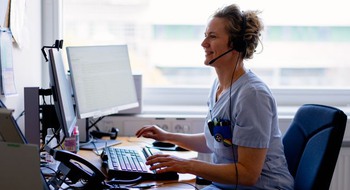 Två personer i skyddskläder framför små plantor i växthus.