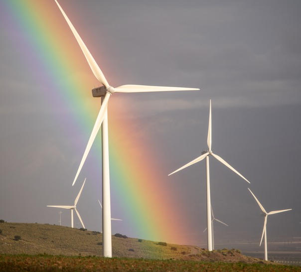 Vindkraftverk med molnig grå himmel och en regnbåge.