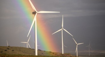 Vindkraftverk med molnig grå himmel och en regnbåge.